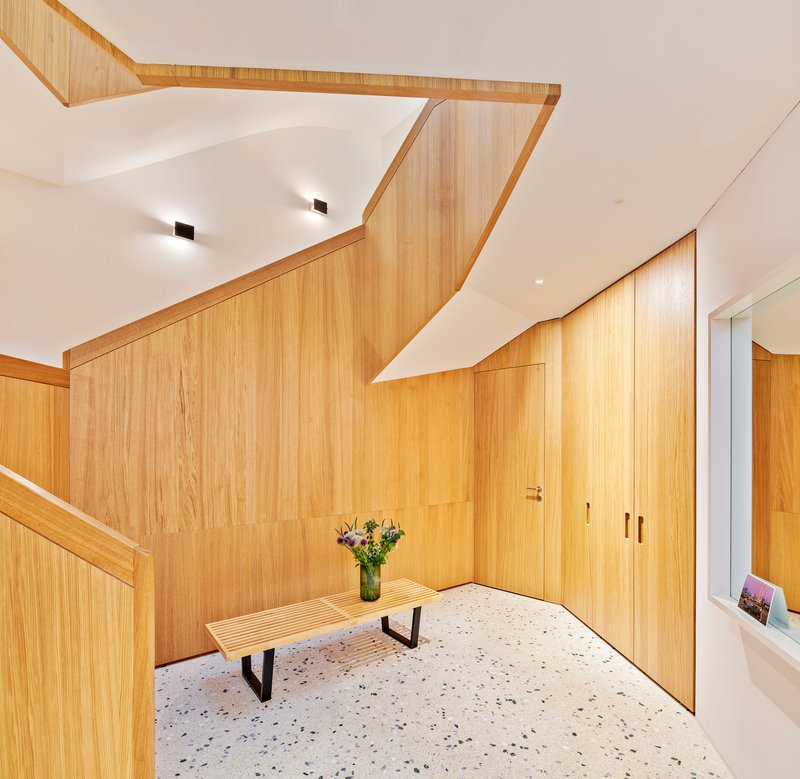 Entry hall with faceted timber-clad wall and ceiling volumes wrapping the staircase