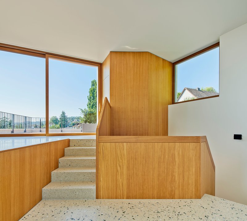 Terrazzo staircase with timber balustrade wrapping around a corner window overlooking distant rooftops