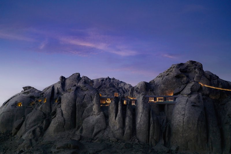 Illuminated window openings carved into the volcanic stone cliff face at twilight