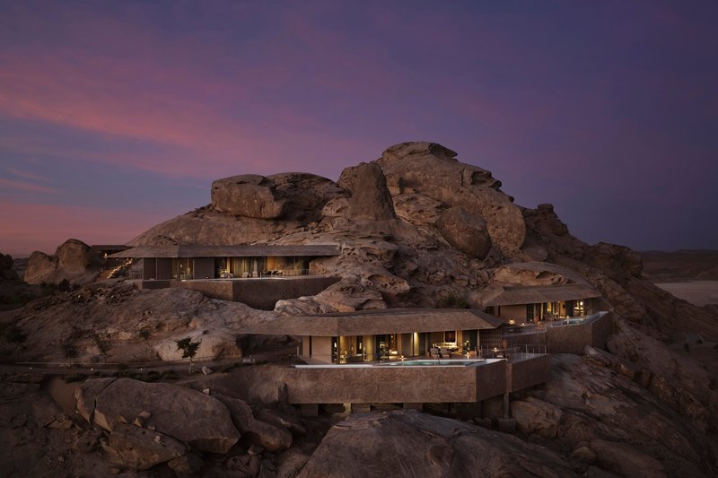 Two-level horizontal structure embedded into the rocky hillside with glazed facades lit at dusk