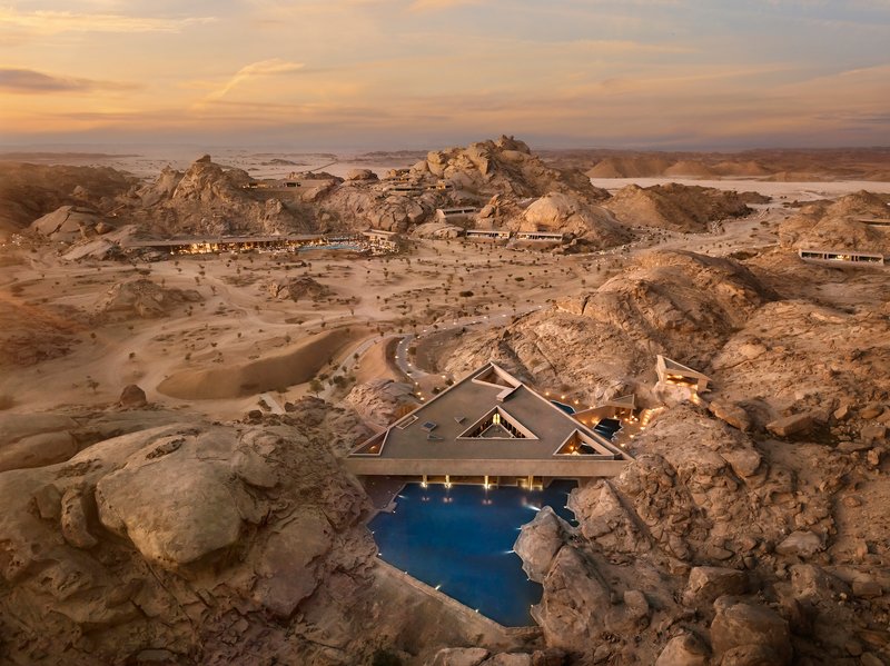 Triangular pool pavilion with cantilevered roof set among boulder formations in the desert at sunset