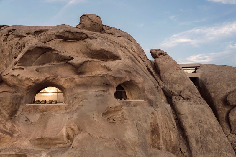 Carved window openings cut into the weathered sandstone boulder under afternoon clouds