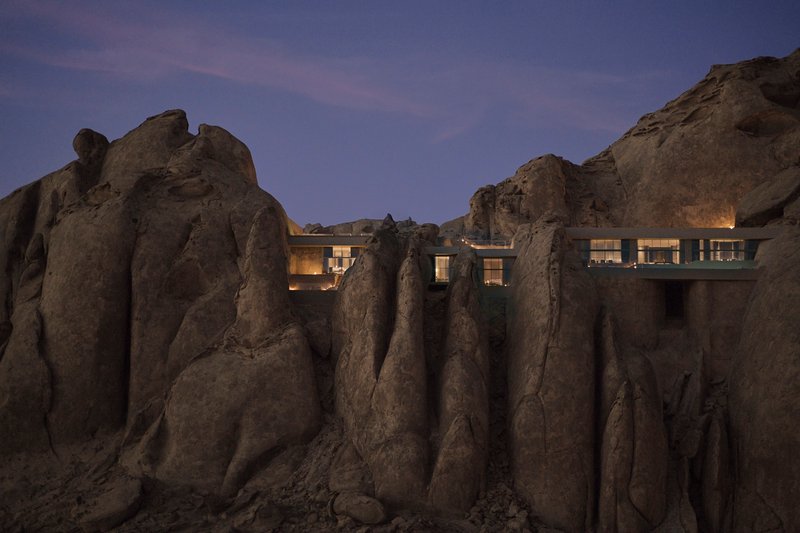 Illuminated glazed openings visible between vertical rock formations at twilight