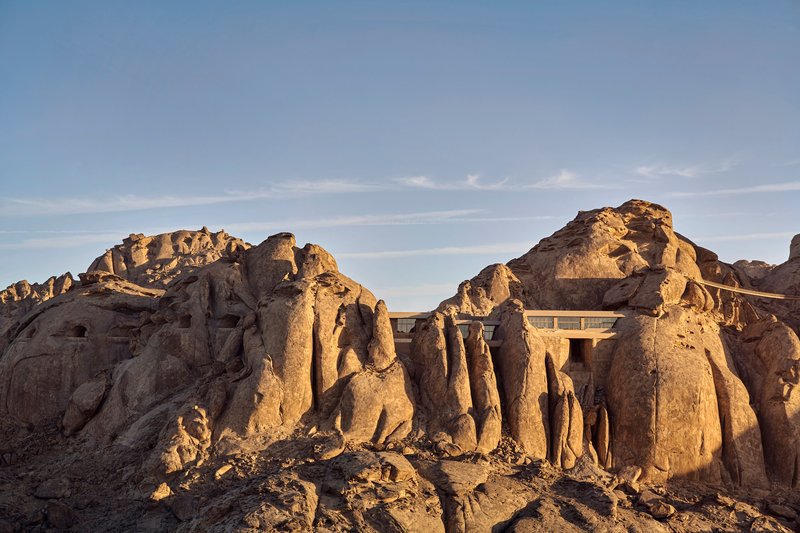 Concrete roof structure rising between jagged rock outcroppings in golden afternoon light
