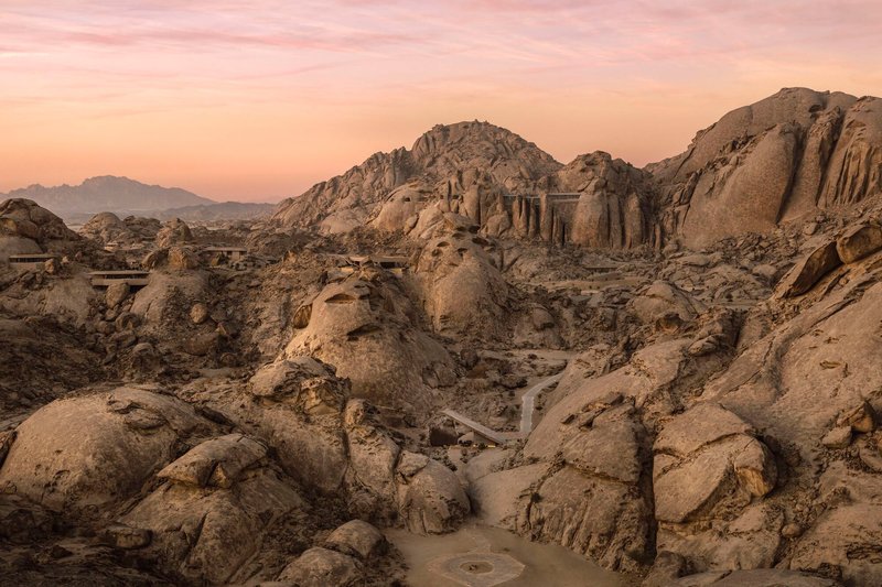 Distant view of structures carved into rocky hillside at dusk with winding pathways below