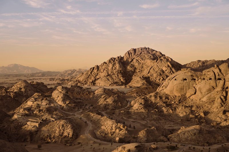 Aerial view of a desert valley with low-rise structures nestled among eroded rock formations at golden hour