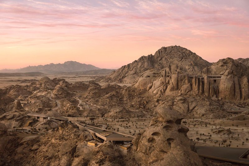 Elevated concrete bridge extending across the desert terrain toward a carved stone outcrop at dusk
