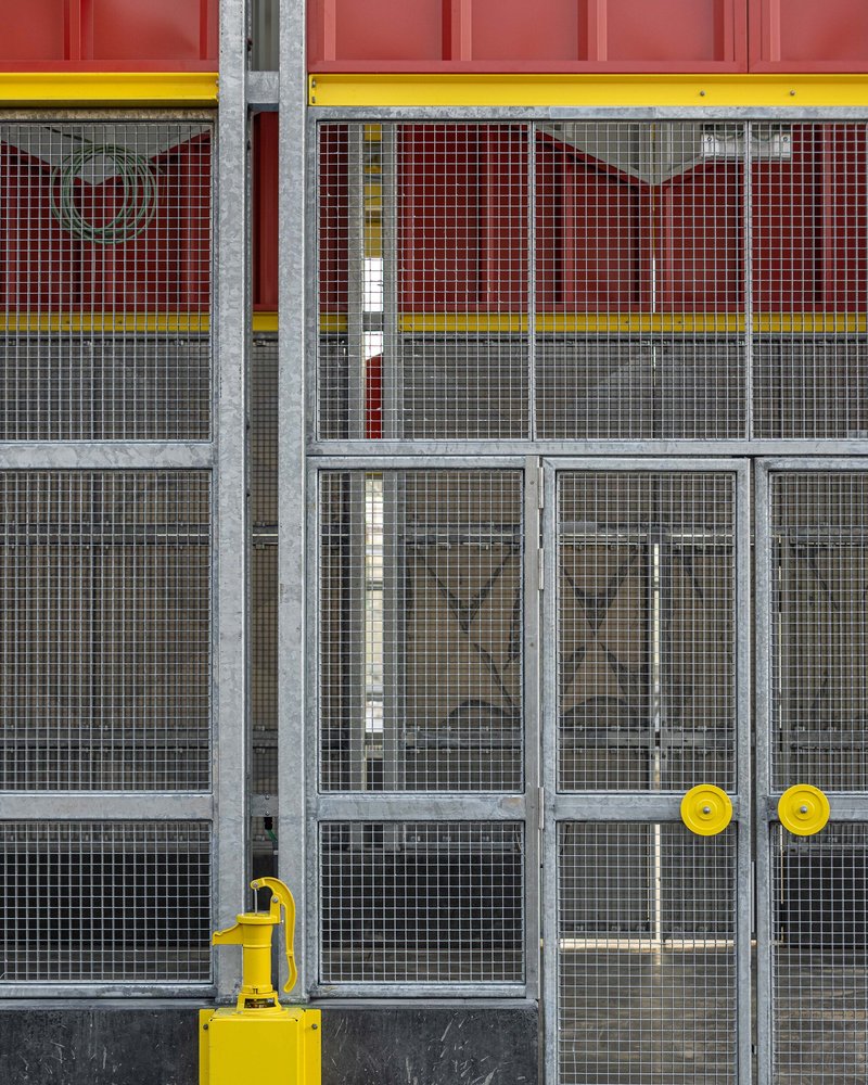 Wire mesh double doors with yellow handles set within red paneling and yellow trim bands