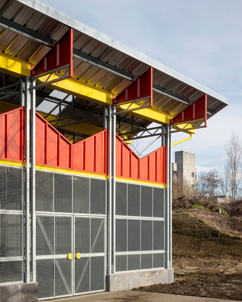 Facade showing red panels, mesh screens, and overhanging roof with bare trees in the background