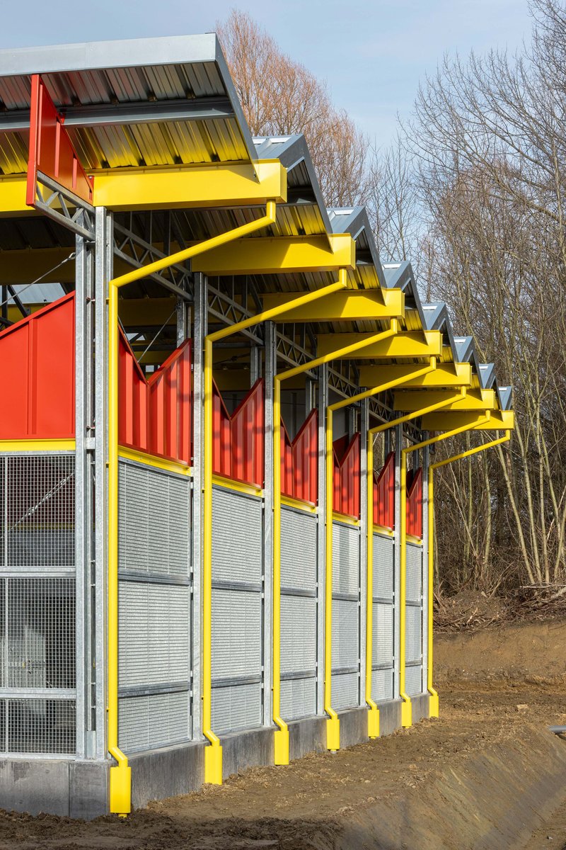 Sawtooth roof edge with yellow beams extending along the facade near winter trees
