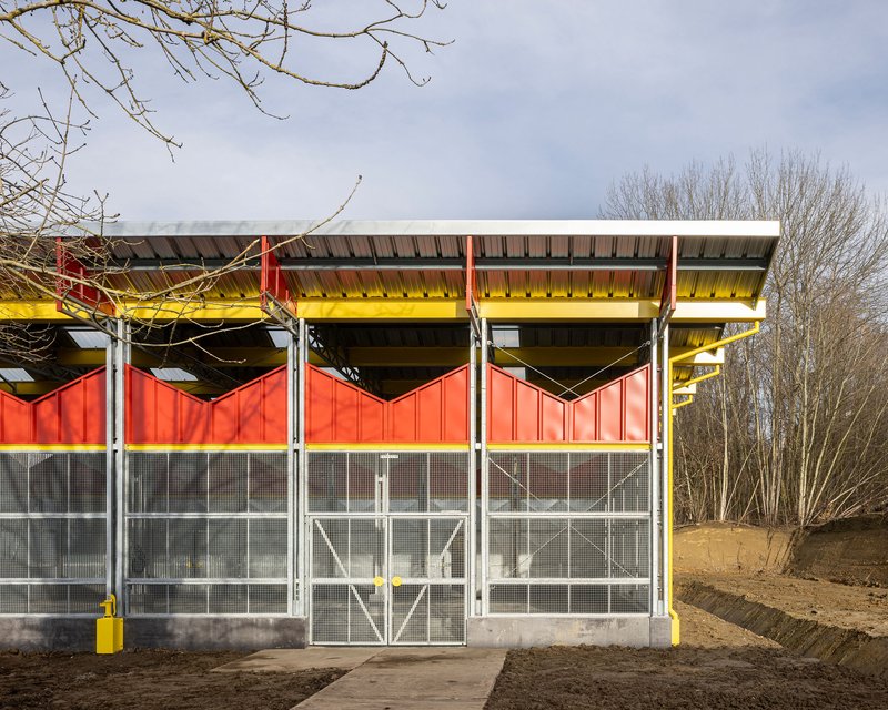 Elevation showing the galvanized mesh walls and red upper panels under bare winter trees