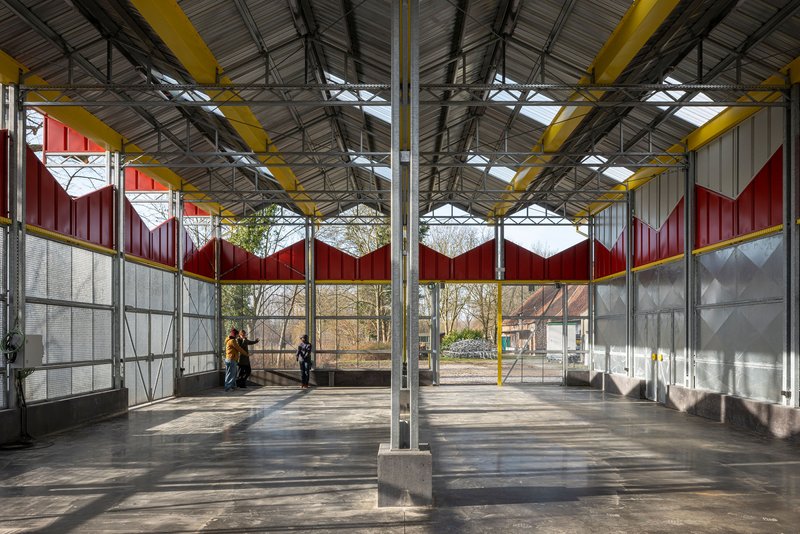 Interior space with exposed steel trusses and yellow columns beneath the corrugated metal roof with skylights