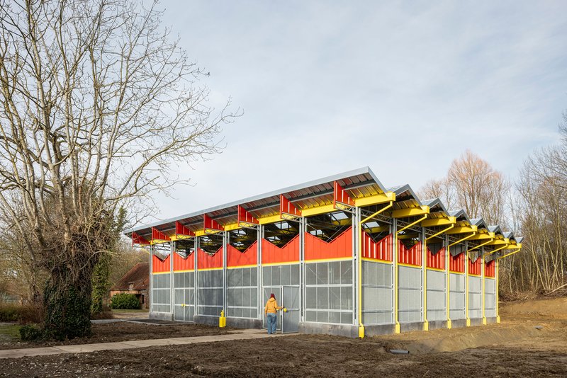 End view of the pavilion with a person standing on the gravel forecourt in winter light