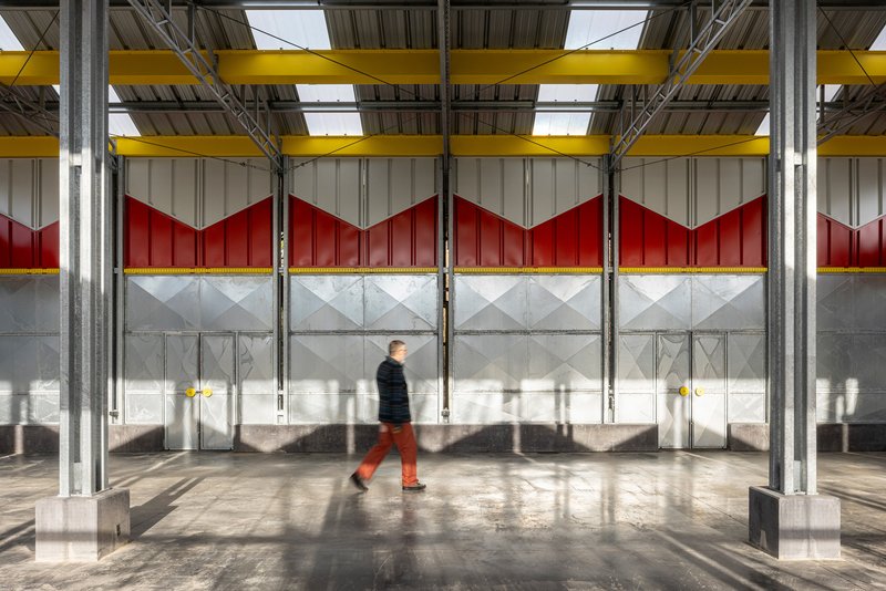 Interior view of mesh wall panels with chevron red and white infill as a figure walks through sunlight