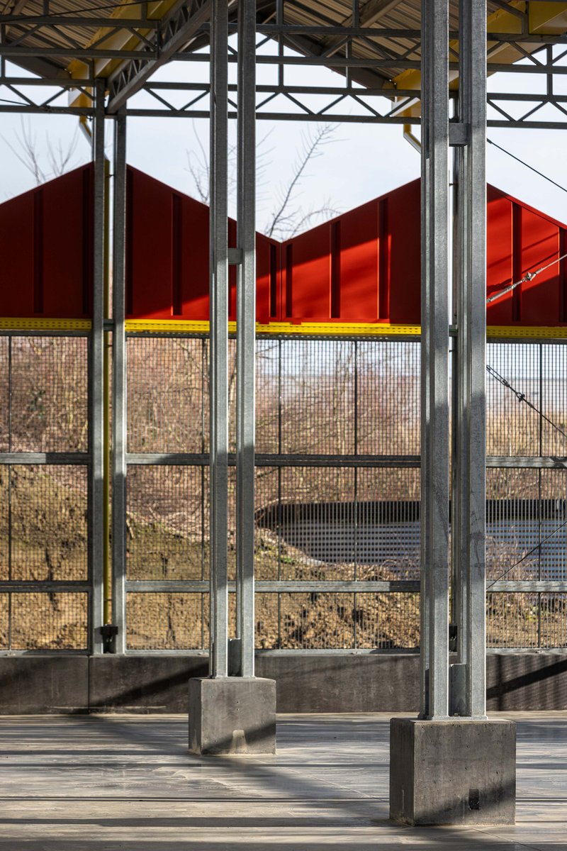 Interior perspective through steel columns on concrete plinths toward mesh walls and winter vegetation beyond