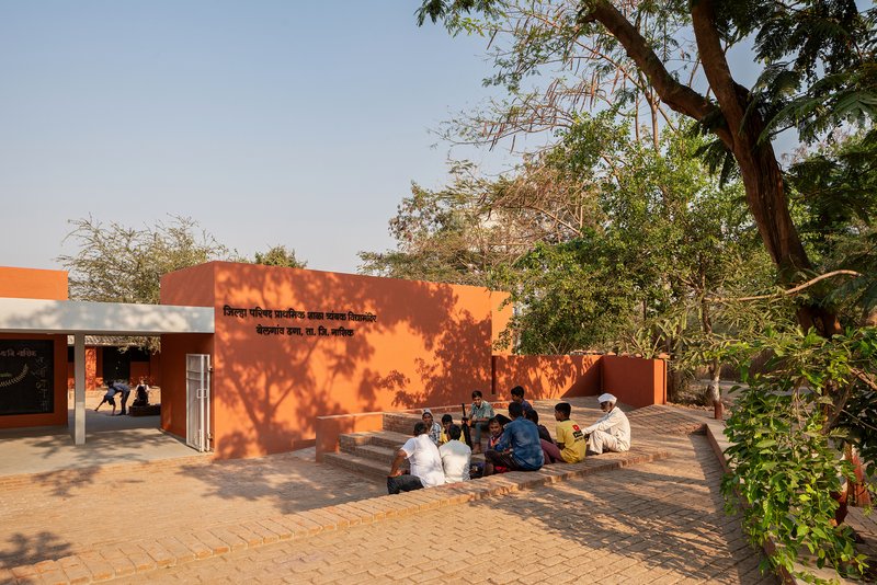 Brick-paved courtyard with orange painted walls and tree shadows cast on the facade