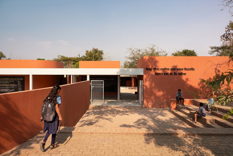 Entrance gate with metal grille between orange walls as a student walks along the pathway