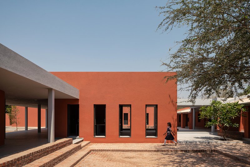 Orange facade with three tall openings overlooking a brick-paved courtyard under midday sun