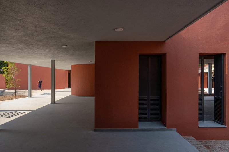 Covered walkway with circular columns and textured ceiling opening to orange walls with louvered doors