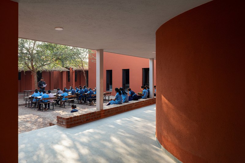 Shaded colonnade overlooking students seated at tables in a brick-paved outdoor courtyard