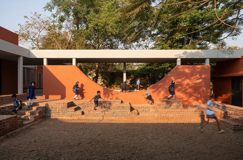 Brick amphitheater steps beneath a white beam with children running in dappled sunlight