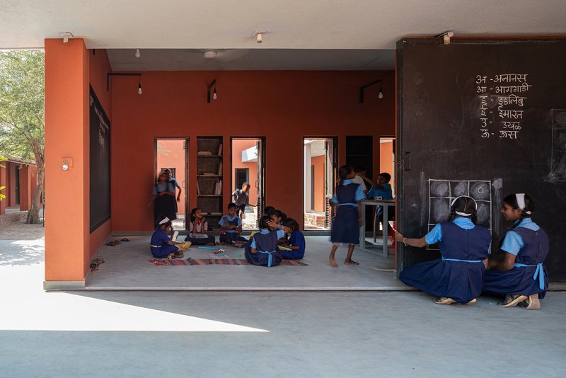 Covered verandah with terracotta and grey columns overlooking sunlit courtyard where students gather in shade
