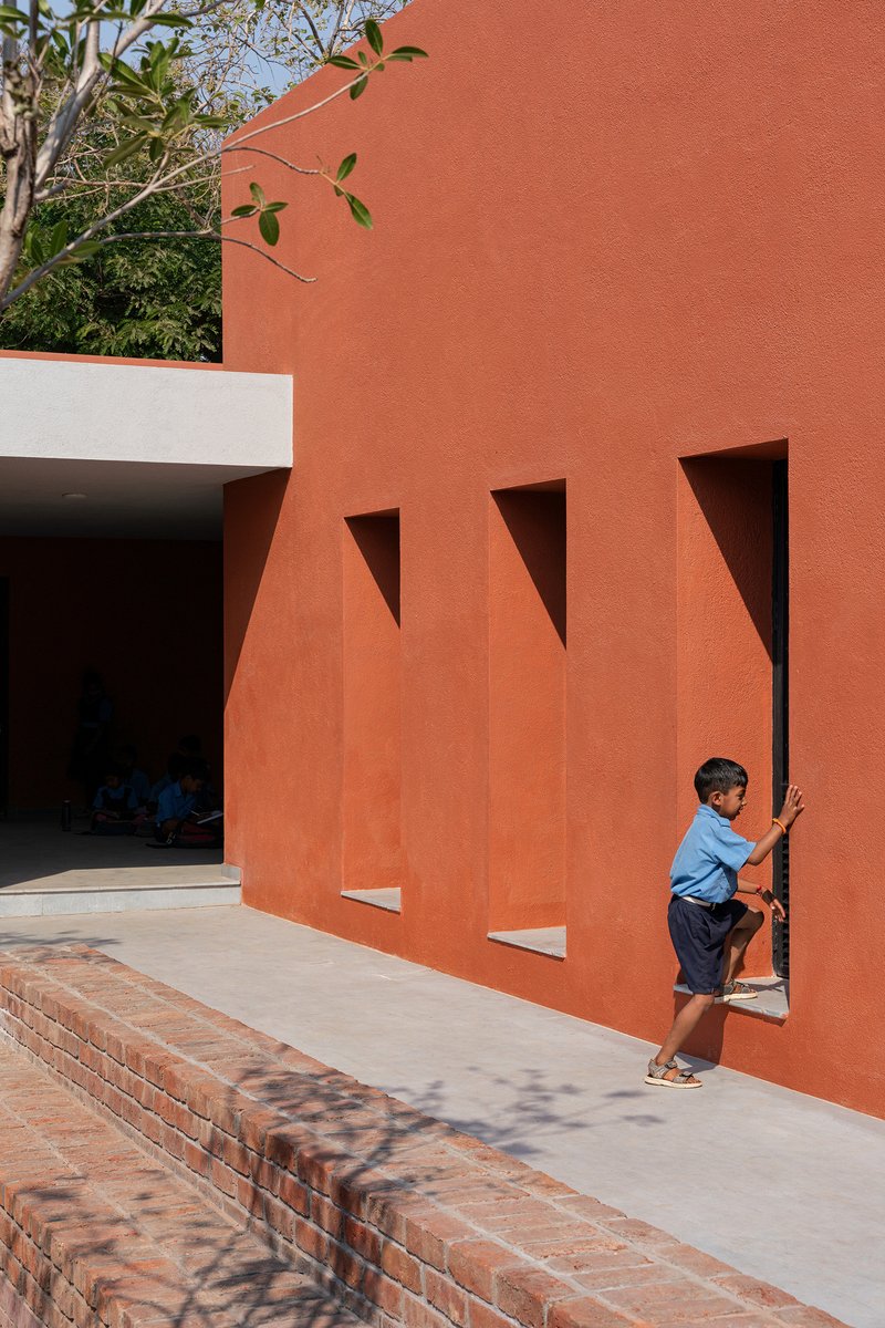 Terracotta screen wall with triangular cutouts filtering sunlight onto paved walkway with brick planter edge