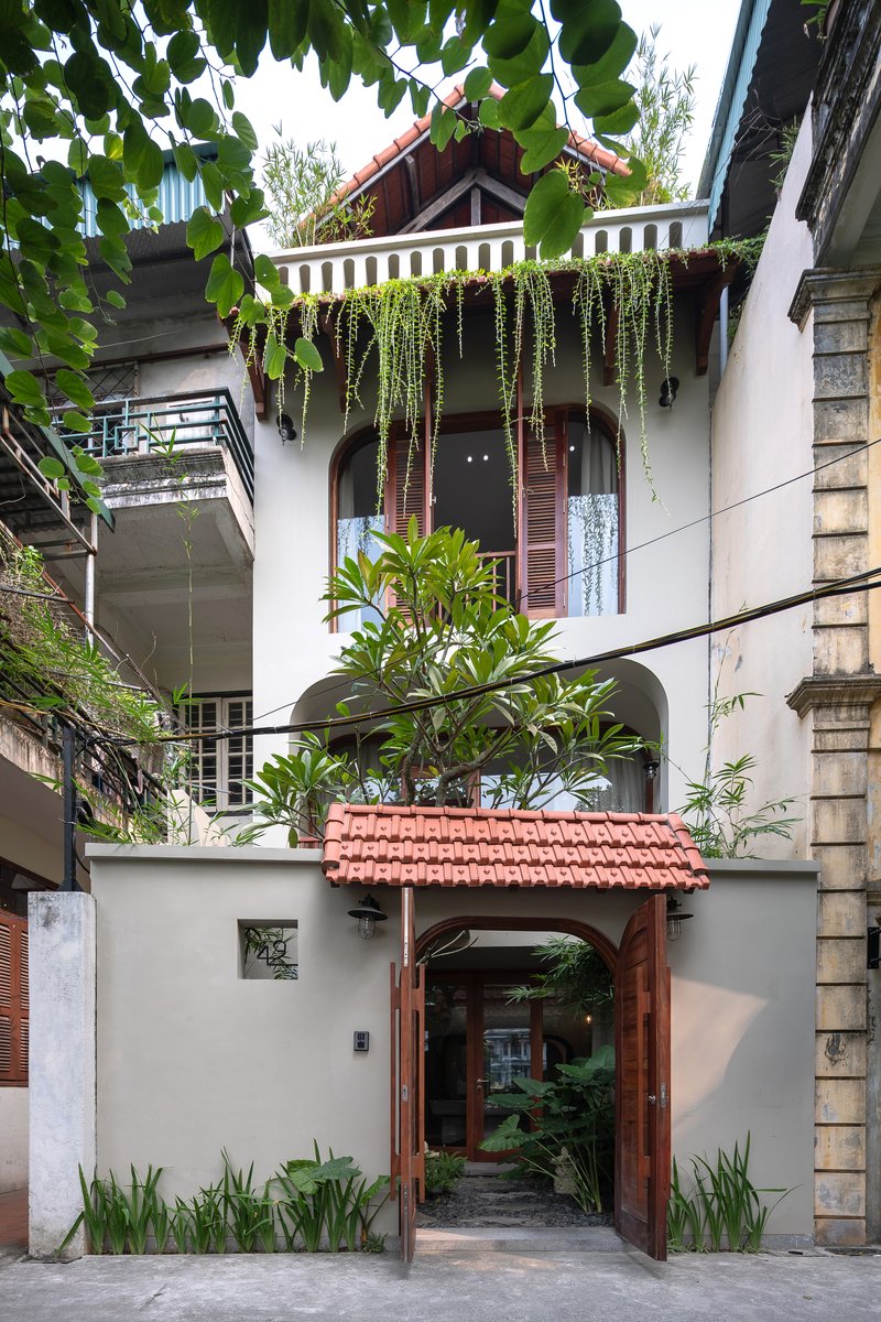 Street facade with timber-framed entry gate, terracotta tile roof and cascading plants from upper balcony