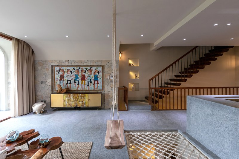 Double-height living space with timber staircase, terrazzo island, and glass floor panel revealing lower level