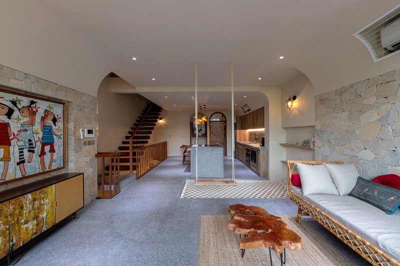 Open-plan living space with stone walls, timber staircase, and rope hammock under recessed ceiling light