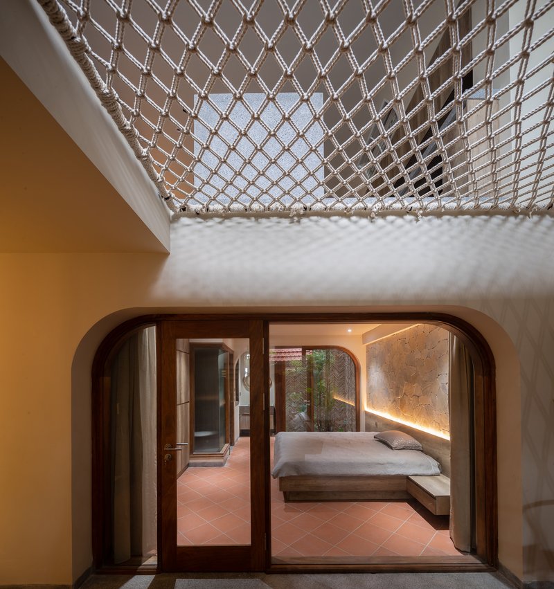 View through rounded timber doorway to bedroom with rope net skylight overhead