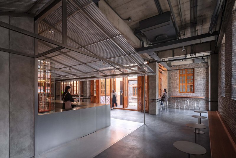 Cafe counter and seating area with exposed structural beams and people moving through the space