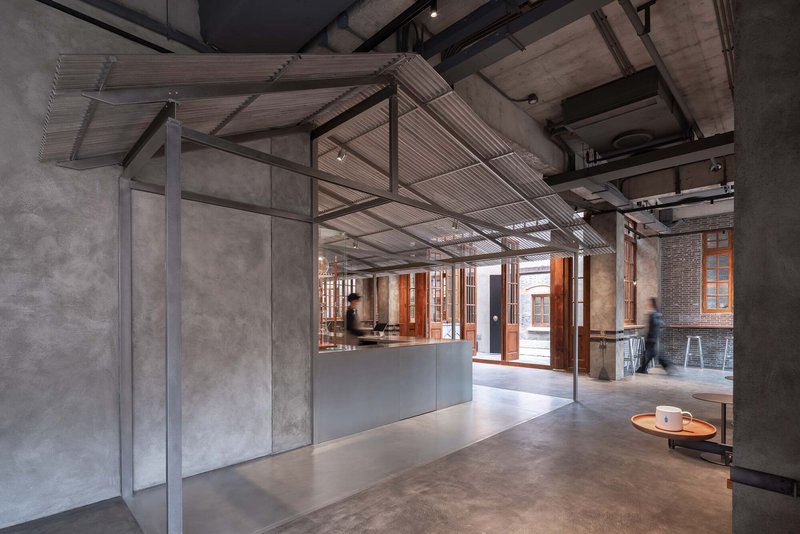 View through steel-framed glass partition toward timber doors with figure in motion beside concrete column