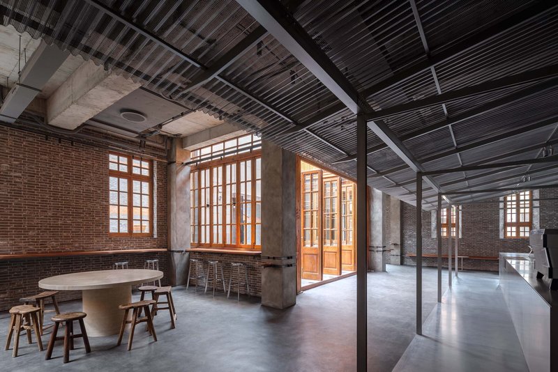 Interior showing corrugated metal ceiling panels, concrete columns, and timber window frames against brick walls