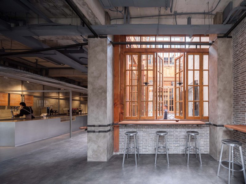 Brick bar counter beneath timber-framed windows with metal stools and a barista working in background