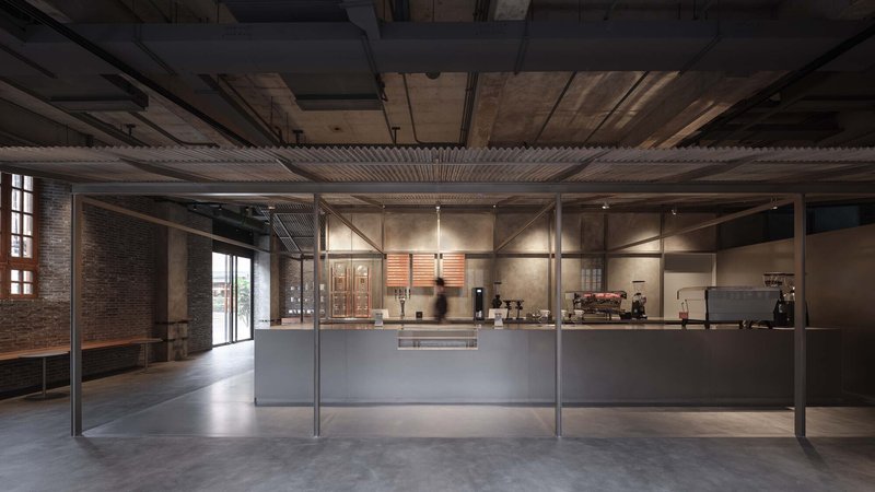 Glass-enclosed coffee counter with corrugated metal canopy in an industrial interior with exposed brick and concrete