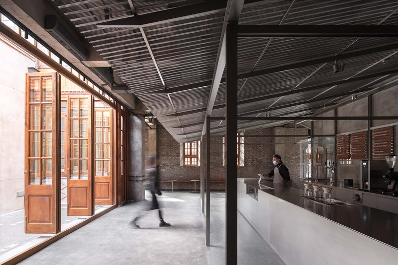 Interior corridor with polished concrete floor, timber doors, and corrugated metal ceiling as a patron walks past