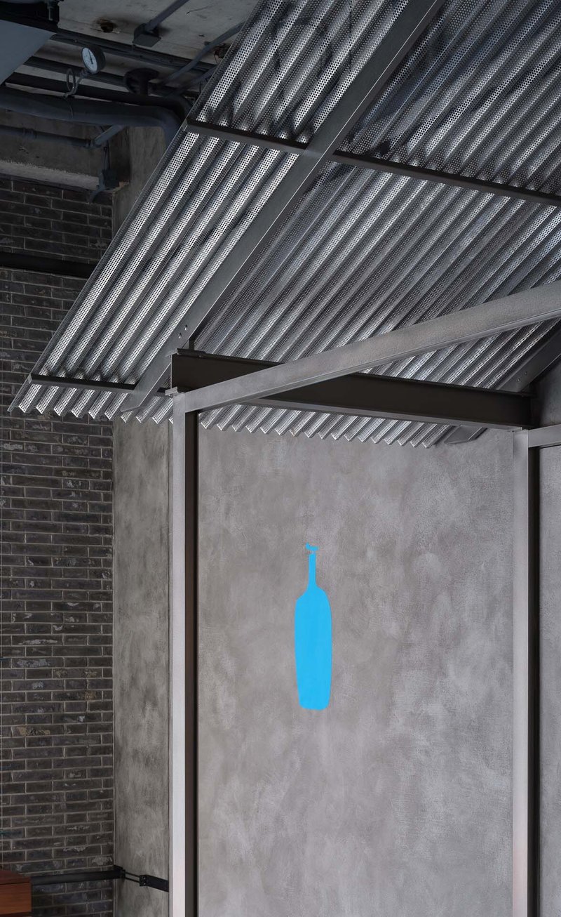 Concrete panel with blue bottle silhouette beneath corrugated metal ceiling and exposed brick wall