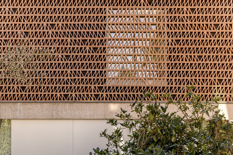 Timber lattice facade with diagonal bracing pattern above planted garden beds at dusk