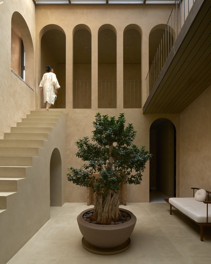 Central atrium staircase with arched niches and a potted tree under a slatted timber ceiling