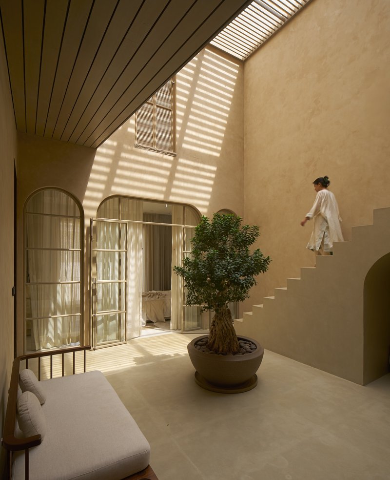 Double-height interior courtyard with slatted skylight casting striped shadows as a person ascends the staircase