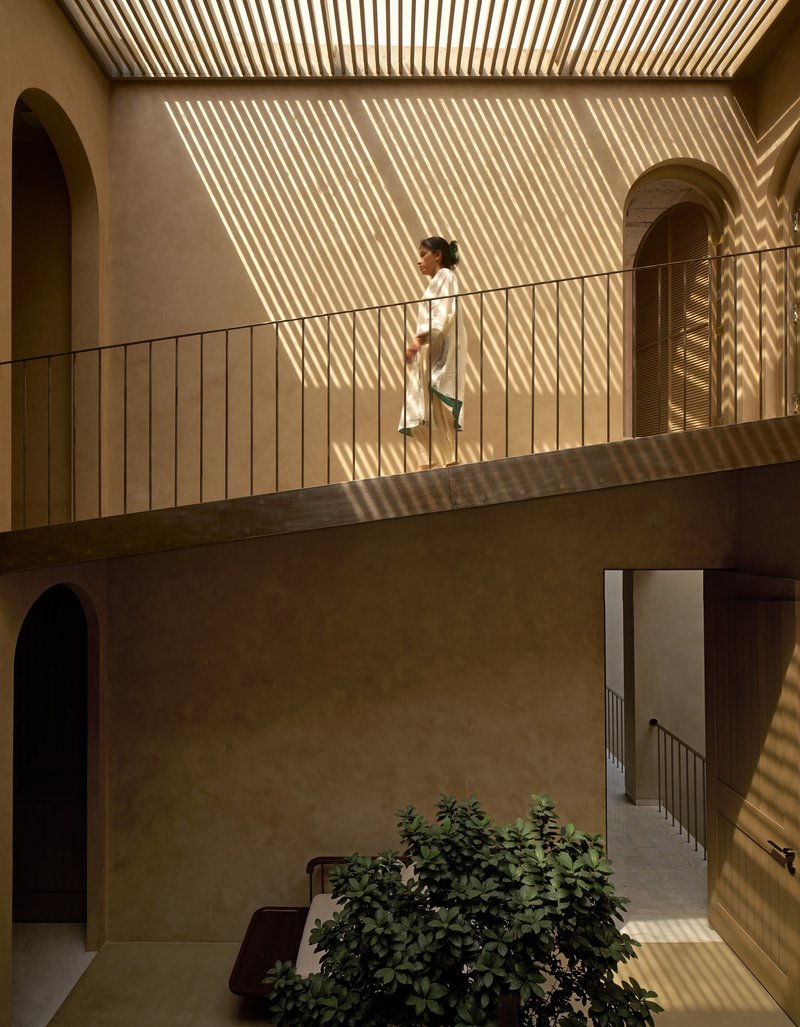 Upper level walkway with metal railing under a slatted timber ceiling casting diagonal shadow patterns