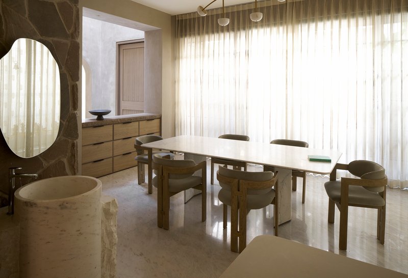Dining area with timber table and chairs beside a dark marble portal and sheer curtain wall