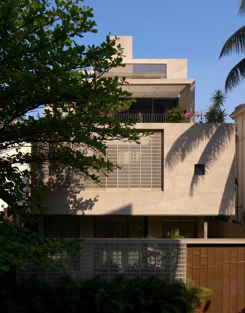Street facade with stacked volumes and gridded brickwork screens framed by palms and tropical trees