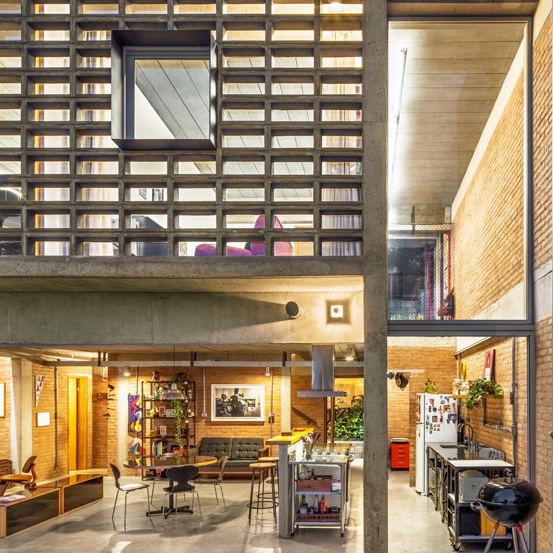 Double-height interior showing concrete columns, brick walls, and grid screen facade lit at dusk