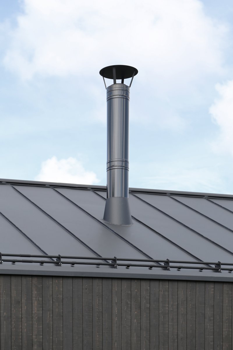 Stainless steel chimney pipe rising from a standing seam metal roof against a cloudy sky