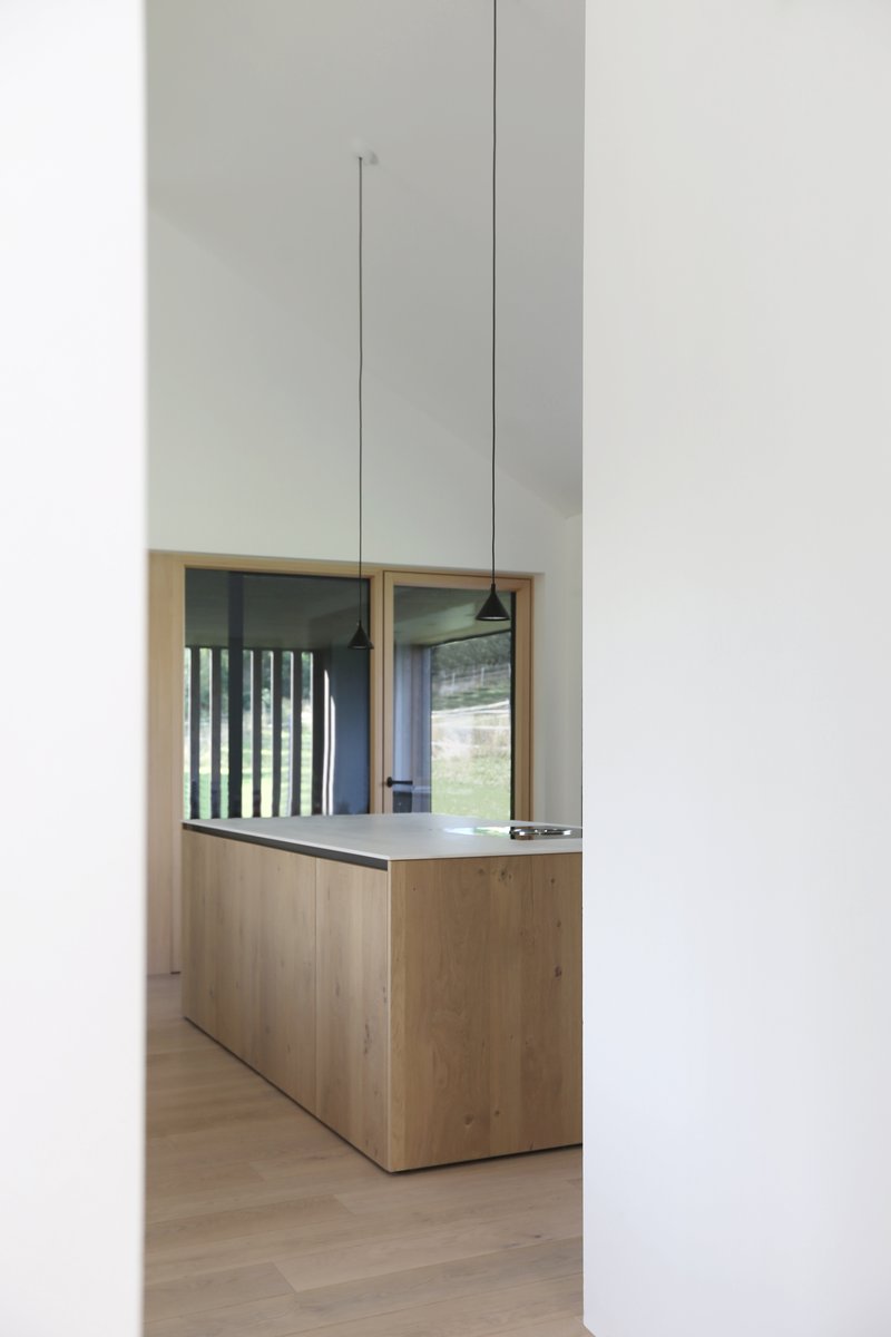 View through doorway to timber kitchen island with mirrored backsplash and pendant lighting