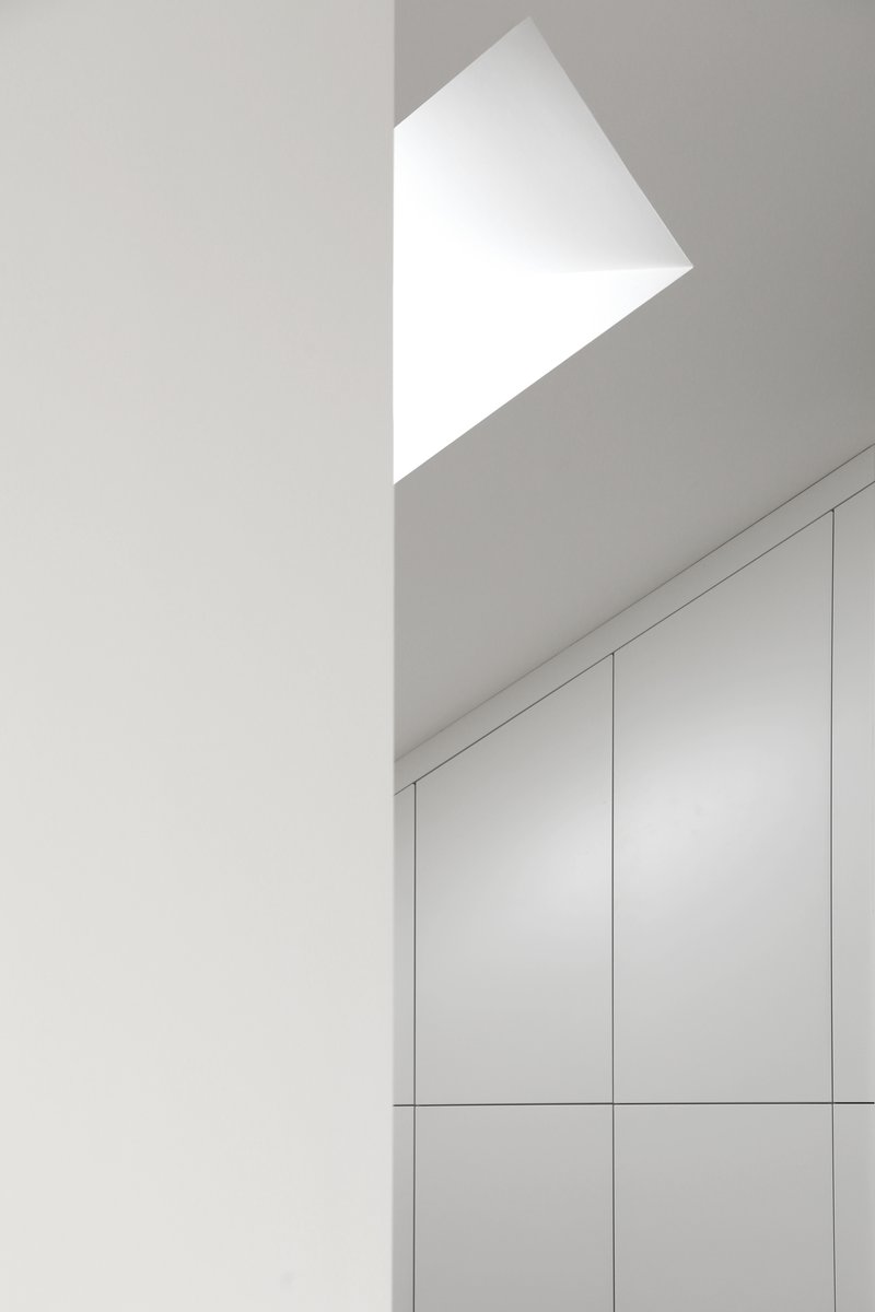 Angular skylight above white built-in cabinetry casting geometric shadows on the ceiling
