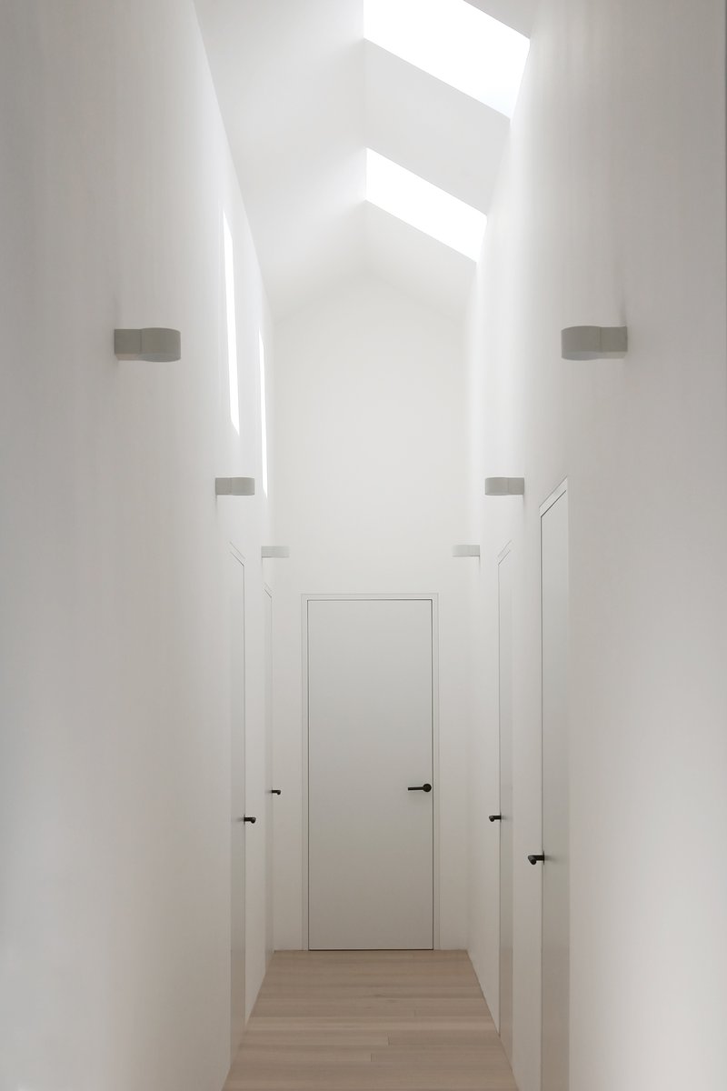 Narrow white hallway with concealed wall sconces and multiple skylights casting bright geometric shadows