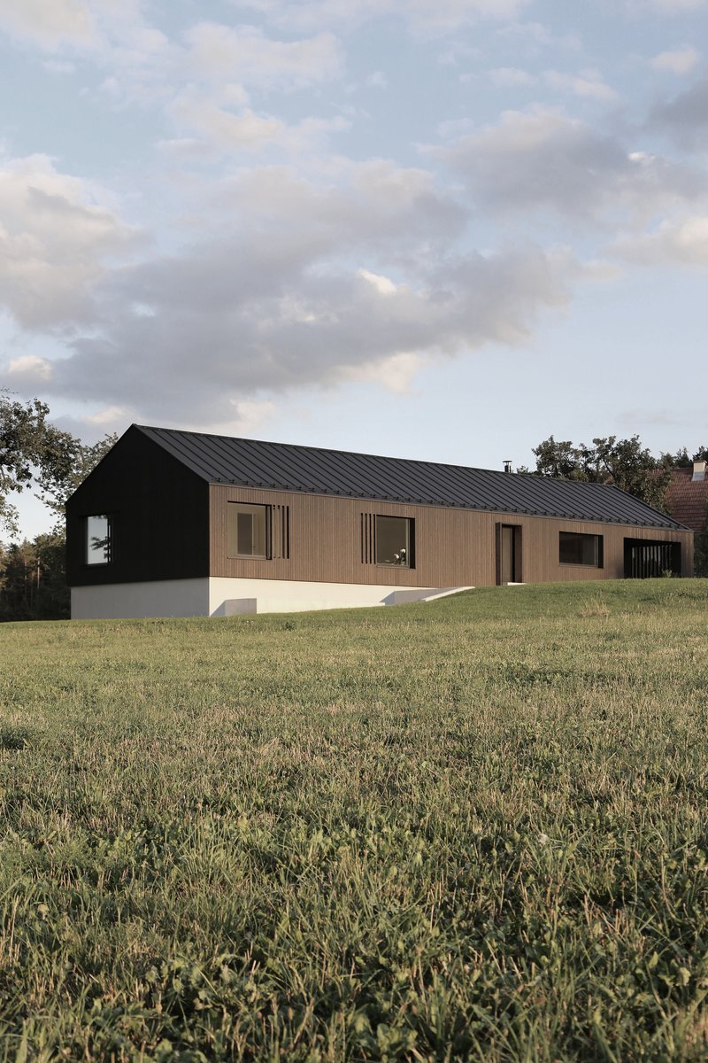 Long elevation showing the dark metal gable roof extending across black and timber-clad facades at dusk